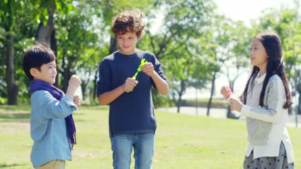 tres niños uno caucásico dos asiático jugando soplando burbujas al aire libre en parque
 - Imágenes, Vídeo
