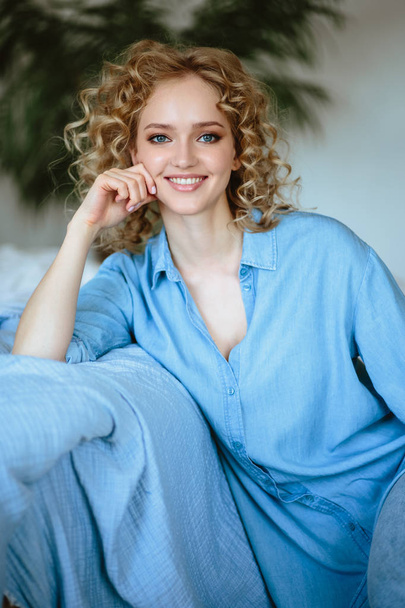 Pretty cheerful blonde young woman with curly hair and charming smile resting in her home, room with modern scandinavian interior - Foto, imagen