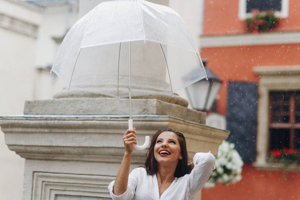 Young and happy woman tourist walking on city street under umbrella, standing near the column. - Foto, imagen