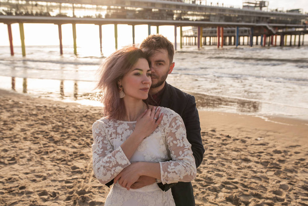 抱擁の若くて美しい夫婦は、ビーチで日没時に結婚式を祝っています - 写真・画像