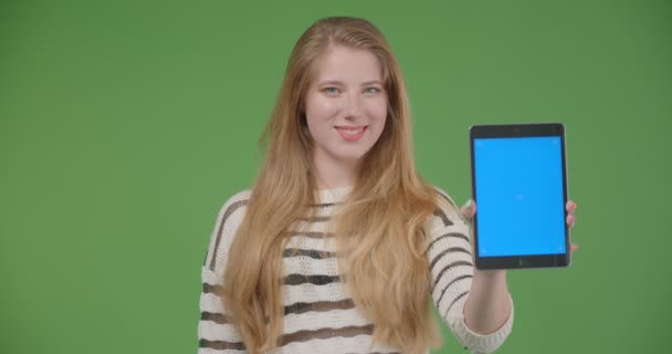 Closeup shoot of young pretty caucasian female using the tablet and showing blue chroma key screen to camera with background isolated on green - Кадры, видео