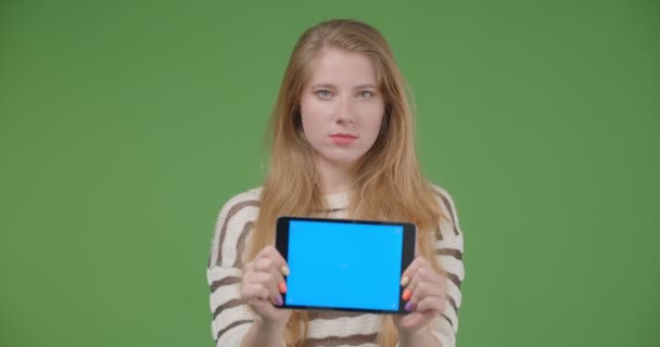 Closeup shoot of young pretty caucasian female using the tablet and showing blue chroma key screen to camera holding it horizontally with isolated background - Video