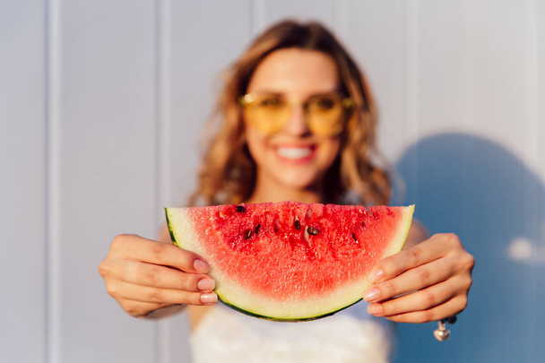 Blurred image of attractive girl standing with piece of watermelon, outside. - Foto, afbeelding