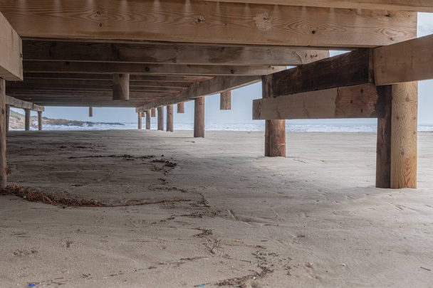 Unterteil einer rustikalen Holzterrasse auf Sand vor dem Meer - Foto, Bild