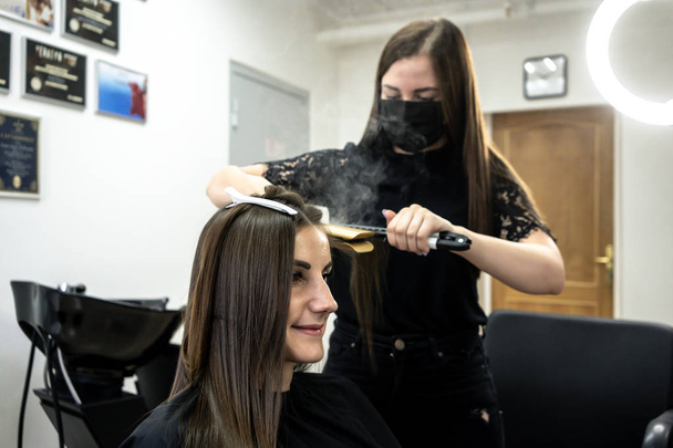 Kadeřník dělá v kadeřnictví krásné vlasy pro dívku s brunetou. koncepce péče o vlasy. - Fotografie, Obrázek