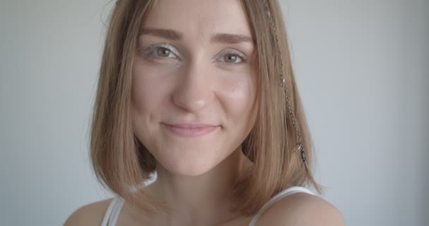 Κοντινό γύρισμα της νεαρής όμορφο καυκάσιο θηλυκό με δαχτυλίδια μαλλιών και λάμψη μακιγιάζ χαμογελαστή κοιτάζοντας την κάμερα στο λευκό δωμάτιο σε εσωτερικούς χώρους - Πλάνα, βίντεο