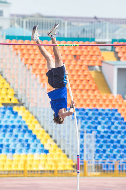 Le saut à la perche - un homme athlétique barbu se repose contre le sol sur le poteau et prêt à sauter par-dessus
 - Photo, image