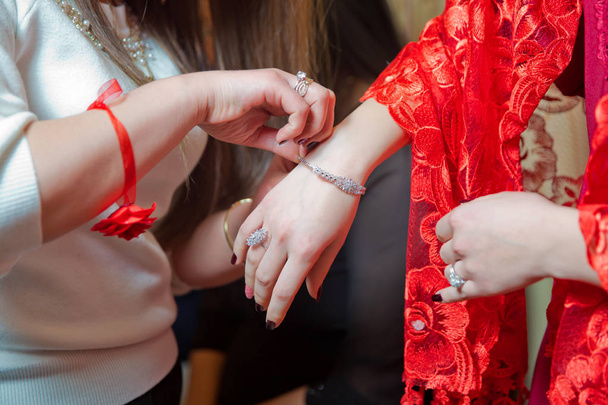 Bridesmaid helps to put a bracelet on his arm for the bride. bride putting on jewelry, focus on bracelet. Close up of groom giving his bride bracelet as symbol of his love on their henna day. - Φωτογραφία, εικόνα