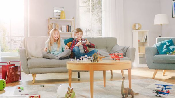 At Home: Smart Boy Playing in Video Game Console, Using Joystick Controller, His Older Sister Sits Near on Sofa and Cheers for Him. Happy Children Playing Videogames Together. - Φωτογραφία, εικόνα