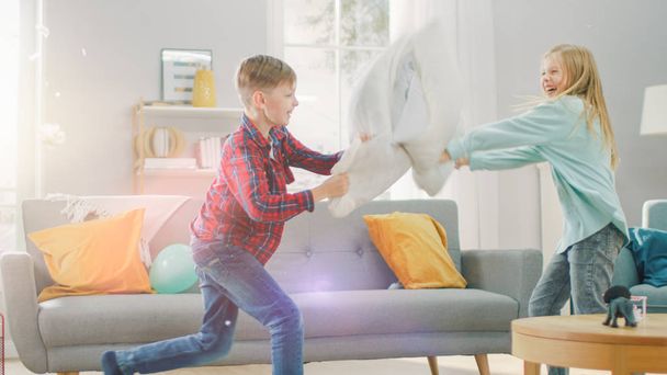 Adorable Little Boy and Sweet Little Girl Have a Pillow Fight in the Sunny Living Room. Siblings Having Fun Fighting with Pillows, Feathers Flying Around. - Photo, image