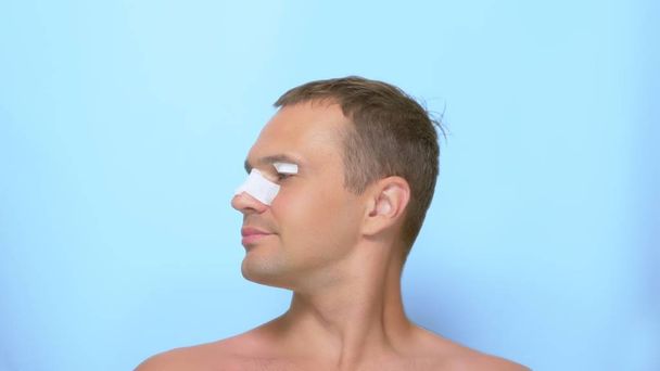 The concept of plastic surgery, a man after a plastic surgery on the face, rhinoplasty and blepharoplasty, with a bandage on the nose and eyelids. on blue background. - Photo, image
