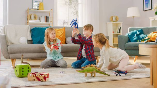 V obývacím pokoji: chlapec a dívka hrají s Hračkářama a dinosaury, když sedí na koberci. Slunný obývací pokoj s dětmi zábava. - Fotografie, Obrázek
