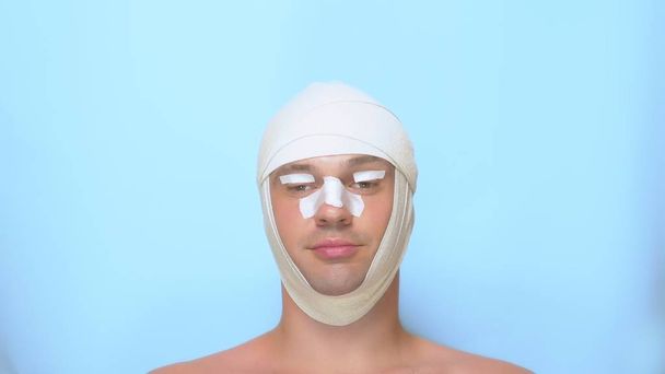 a man after a plastic surgery facelift, rhinoplasty, blepharoplasty. with a bandage on the nose, head and eyes. on blue background. shows a super sign and okay - Zdjęcie, obraz