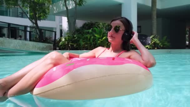 Gelukkige vrouw en opblaasbare zwem ring in de vorm van een donut in het zwembad en luistert naar muziek in de winkel. - Video