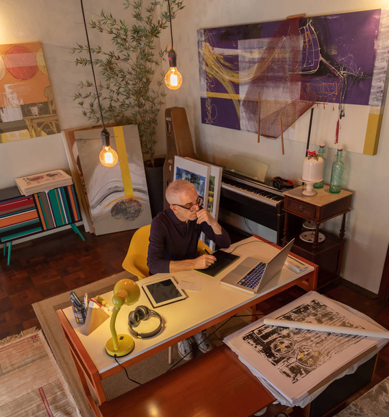 Homme d'âge moyen utilisant un ordinateur dans son atelier d'art et dessinant sur sa tablette
 - Photo, image