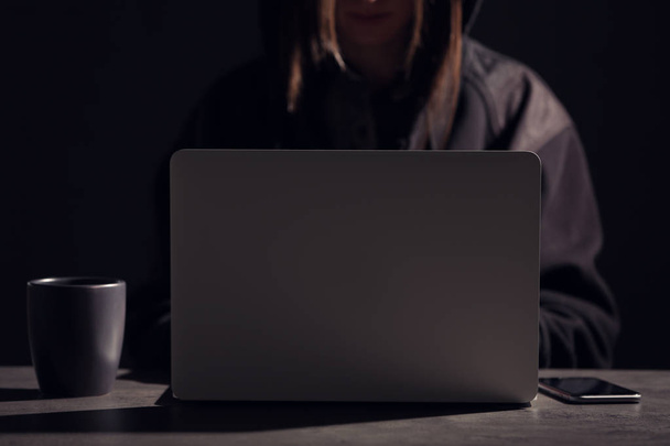 Woman with laptop and smartphone at table in darkness, closeup - Фото, зображення
