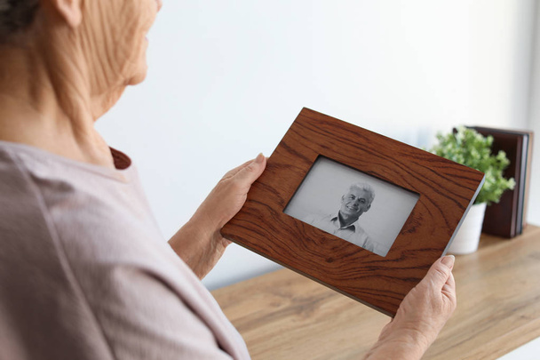 Mulher idosa com foto emoldurada de seu filho em casa
 - Foto, Imagem