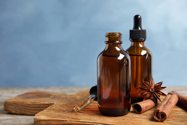 Bottles of essential oils and cinnamon sticks on wooden table against blue background. Space for text - Foto, Imagem