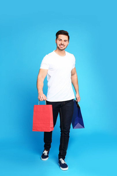 Full length portrait of young man with paper bags on blue background - Φωτογραφία, εικόνα