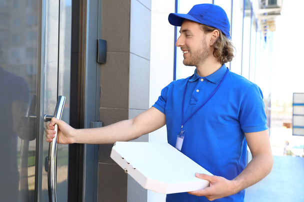 Correo masculino con pizza en la entrada. Servicio de entrega de alimentos
 - Foto, imagen