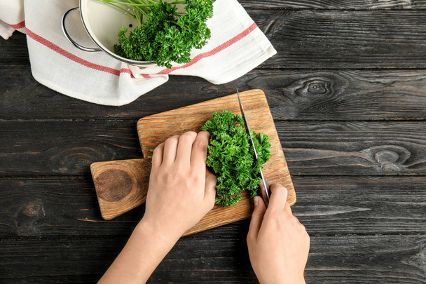 Woman cutting fresh green parsley at dark wooden table, top view - Zdjęcie, obraz
