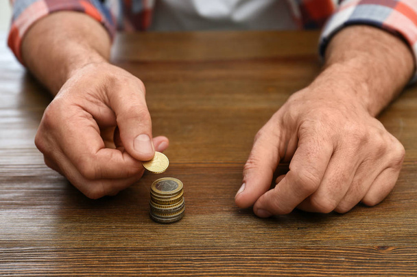 Senior man stacking up coins at table, closeup - Fotó, kép