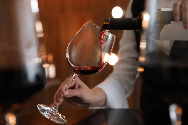 Waitress pouring wine into glass in restaurant, closeup - 写真・画像