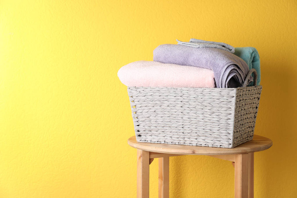 Basket with clean laundry on wooden table near yellow wall, space for text - Φωτογραφία, εικόνα