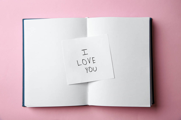 Piece of paper with phrase I LOVE YOU and notebook on pink background, top view - Фото, изображение