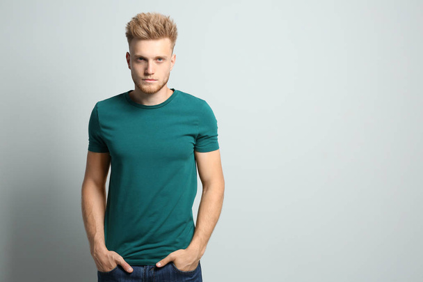 Young man wearing blank t-shirt on light background. Mockup for design - Fotó, kép