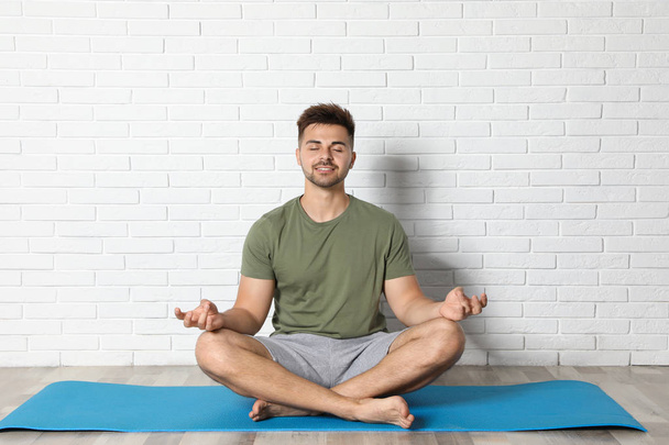 Young man practicing zen yoga near white brick wall - Foto, imagen
