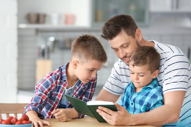 Dad and his sons reading interesting book in kitchen - Фото, изображение