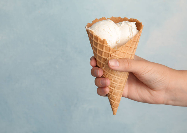 Woman holding delicious ice cream in wafer cone on light blue background, closeup. Space for text - Фото, изображение
