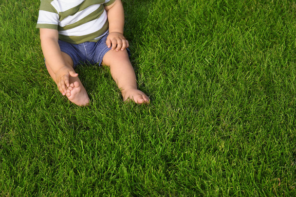 Чарівна маленька дитина сидить на зеленій траві на відкритому повітрі, крупним планом
 - Фото, зображення