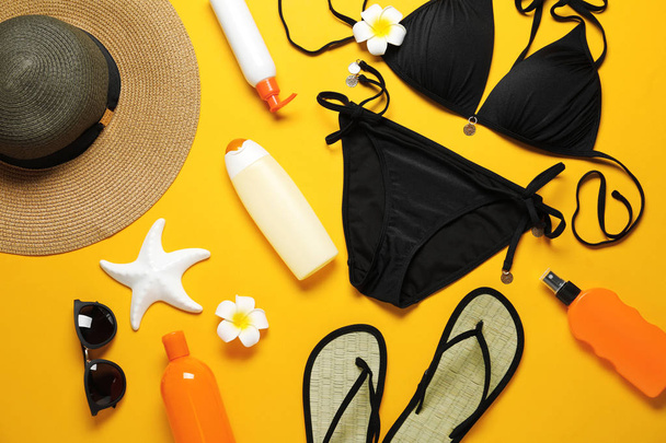 Flat lay composition with black swimsuit and beach accessories on yellow background - Foto, Bild