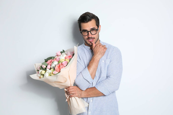 Young handsome man with beautiful flower bouquet on light background - 写真・画像