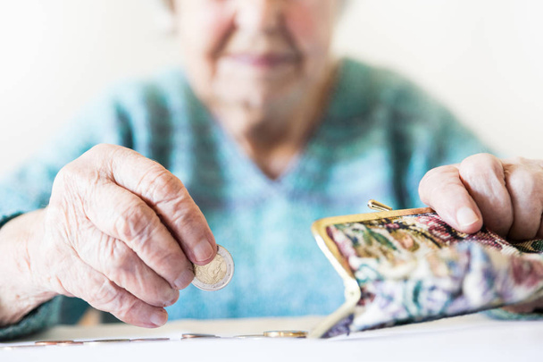 Detailed closeup photo of unrecognizable elderly womans hands counting remaining coins from pension in her wallet after paying bills. - 写真・画像