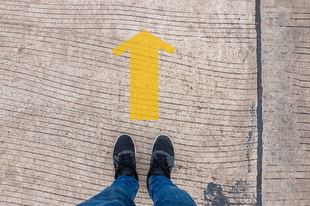 Person wearing sneakers standing on a concrete road with yellow arrows, Decision-making concept - Photo, Image