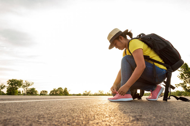 Женщины туристы связывая кроссовки на шоссе с золотым светом солнца, концепция туристов
. - Фото, изображение