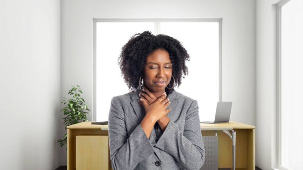 Una mujer de negocios afroamericana negra en una oficina que parece enferma de dolor de garganta. Es propietaria o ejecutiva del lugar de trabajo. Representa las carreras y la creación de empresas
.  - Foto, imagen