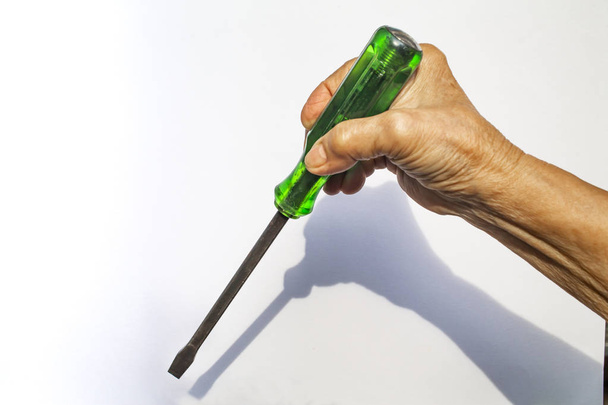 La mano derecha de la mujer mayor sostiene el destornillador verde viejo sobre fondo blanco, construcción y concepto de herramienta de reparación
 - Foto, Imagen