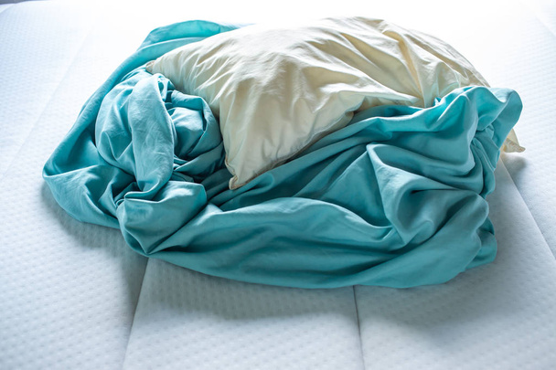 Sábana arrugada turquesa con almohada de marfil en cama blanca, Primer plano, Enfoque selectivo, Concepto de limpieza de dormitorios
 - Foto, Imagen