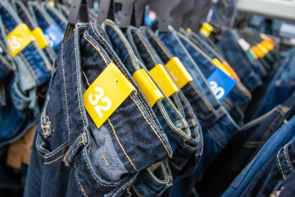 In Großaufnahme hängen viele Jeans auf einem Regal. Reihenweise Jeans-Hosen hängen im Schrank. Konzept von kaufen, verkaufen, einkaufen und Jeans-Mode.  - Foto, Bild