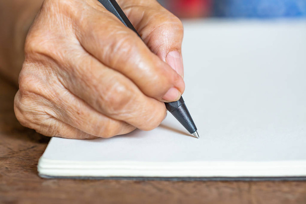 Carta de escritura de mano derecha para mujer mayor sobre fondo de papel marfil, Cuaderno, Un bolígrafo negro, Primer plano y plano macro, Enfoque selectivo, Concepto de papelería
 - Foto, Imagen