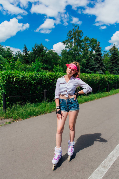 Portrait of an emotional girl in a pink cap visor and protective gloves for rollerblades and skateboarding riding on rollerblades on the road. - Fotografie, Obrázek