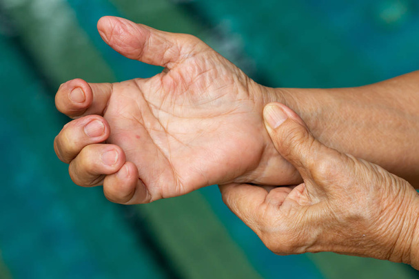 Abzugsfinger, die linke Hand der Seniorin massiert ihre rechte Hand, die unter Schmerzen leidet, Nahaufnahme und Makroaufnahme, Schwimmbadhintergrund, Gesundheitsfürsorge und Massage, asiatisches Körperkonzept - Foto, Bild