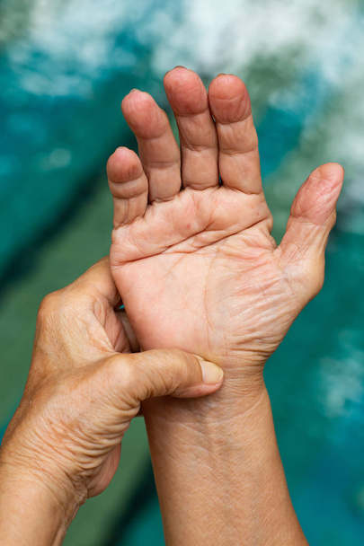 Abzugsfinger, die linke Hand der Seniorin massiert ihre rechte Hand, die unter Schmerzen leidet, Nahaufnahme und Makroaufnahme, Schwimmbadhintergrund, Gesundheitsfürsorge und Massage, asiatisches Körperkonzept - Foto, Bild