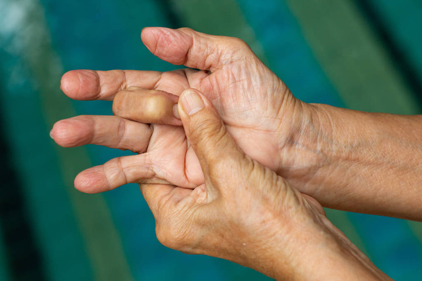 Palec wyzwalacza, Starsza kobieta lewą ręką masując jej środkowy palec, cierpiących na ból, zbliżenie i makro strzał, basen tła, opieka zdrowotna i masaż, koncepcja ciała azjatyckich - Zdjęcie, obraz
