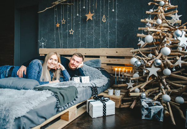 Ρομαντικό ζευγάρι κοιτάζοντας την κάμερα χαλάρωσης κατά τη χειμερινή διακοπές μαζί σε άνετο διαμέρισμα. - Φωτογραφία, εικόνα
