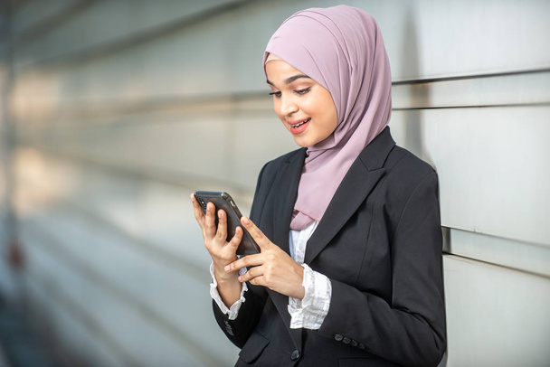 Молодая мусульманская предпринимательница смотрит на свой смартфон. Шал
 - Фото, изображение